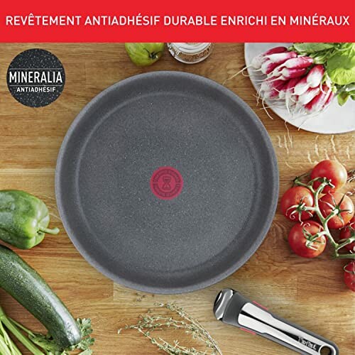 Poêle antiadhésive entourée de légumes frais et ustensiles de cuisine.